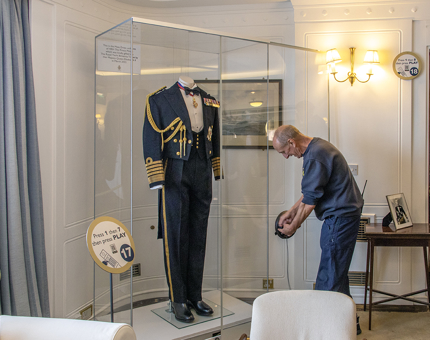 A man from the Facilities Team opens a glass display cabinet which contains a military uniform.