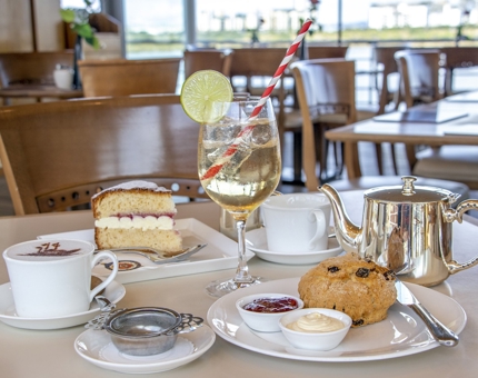 In the Tearoom, a table is set with pot of tea, gin cocktail, scone and a slice of Victoria sponge cake.