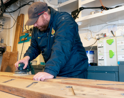 A man from the Maintenance team sanding in the workshop.