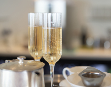 Two glasses of rose sparkling wine and a silver teapot.