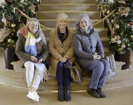 Three ladies sitting on the Grand Staircase with Christmas garlands decorating the handrails.