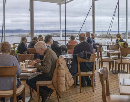 A view of the Royal Deck Tea Room with many visitors sitting at tables enjoying drinks, scones and cakes.