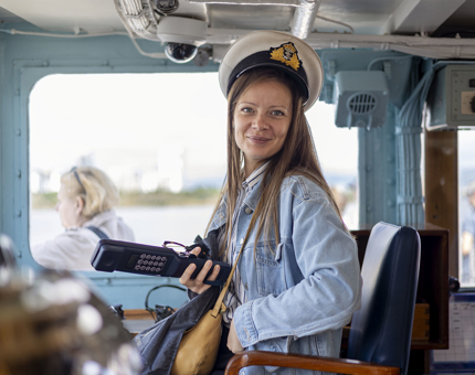 A woman sitting in the Captain's chair in the Bridge, she is wearing a Captain's hat.