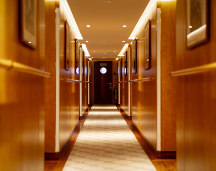 A corridor aboard Fingal Hotel. There is a dark brown door at the end with a circular window.