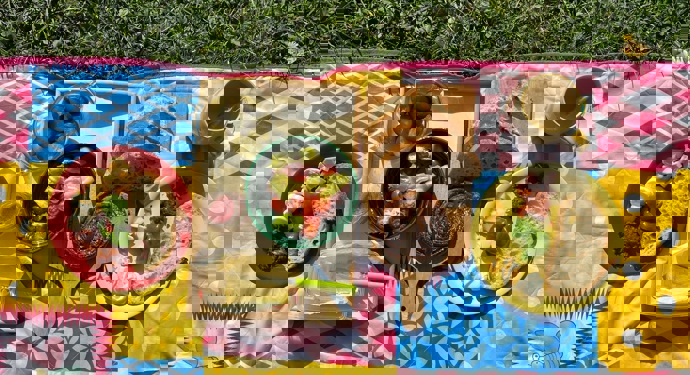 A colourful picnic blanket with plates of food on it.