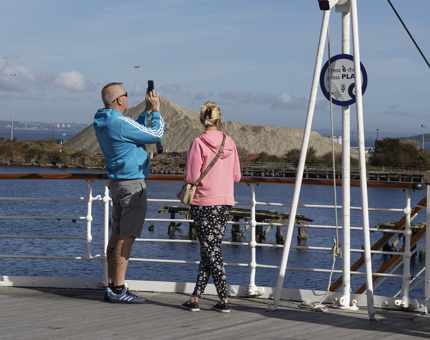 A man and a woman on the Verandah Deck taking a photo of the port.